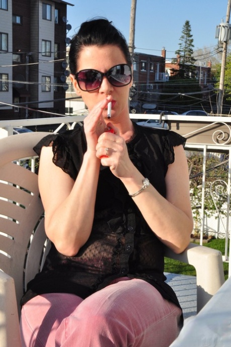 Fully clothed brunette woman smokes and drinks on patio in sunglasses 11059427